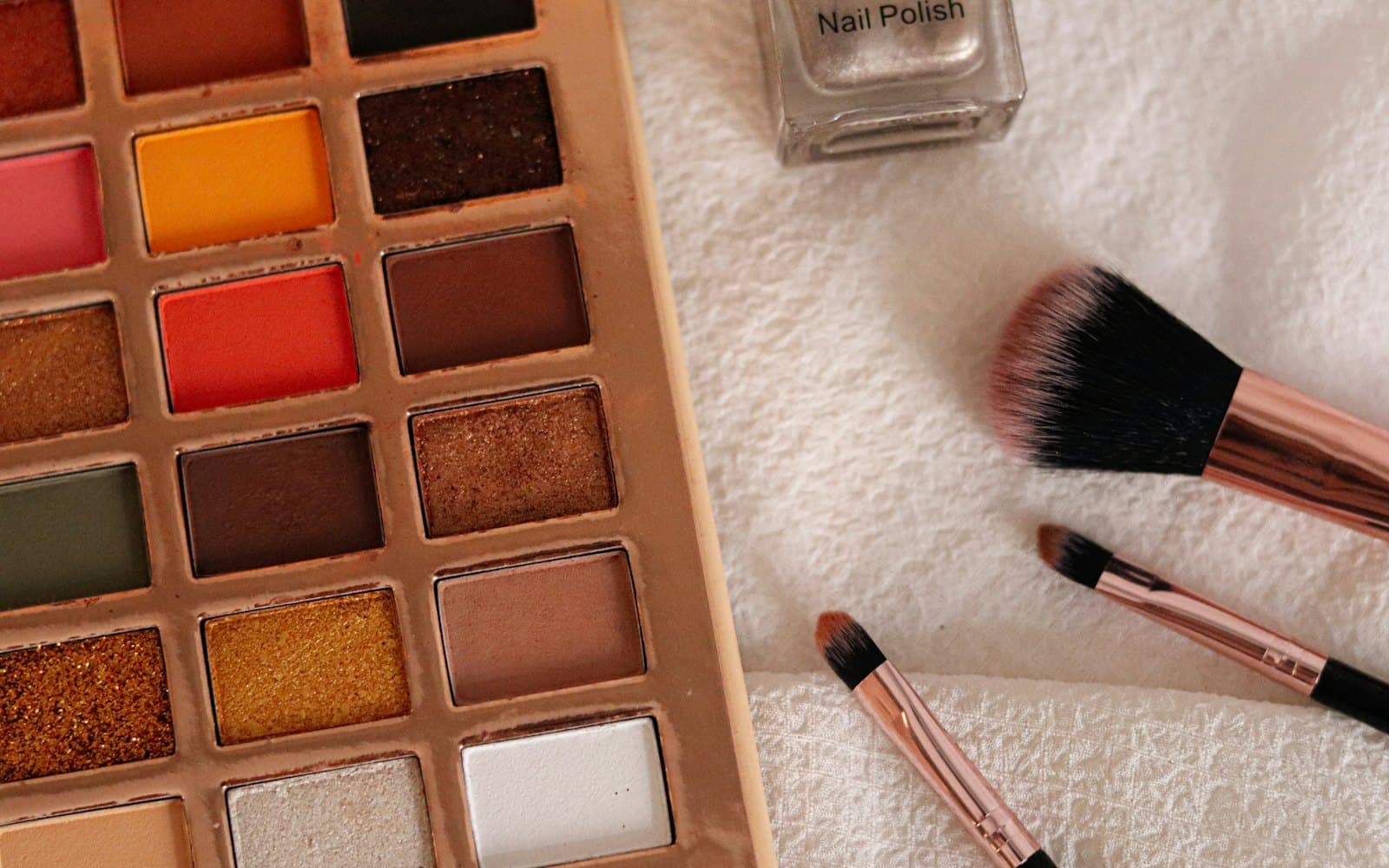 An eyeshadow palette and two brushes on a white towel